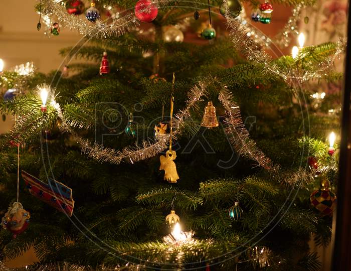 Close-Up Of A Branch Of Christmas Tree With Burning Candles, Wreath, Tinsel Colorful Baubles.