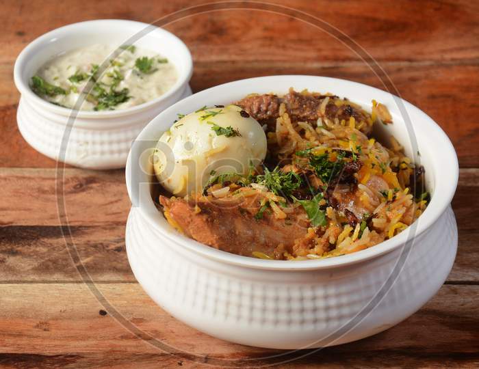 Traditional Hyderabadi Chicken Dum Biryani Made Of Basmati Rice Cooked With Masala Spices, Served With Boiled Egg And Onion Raita, Selective Focus