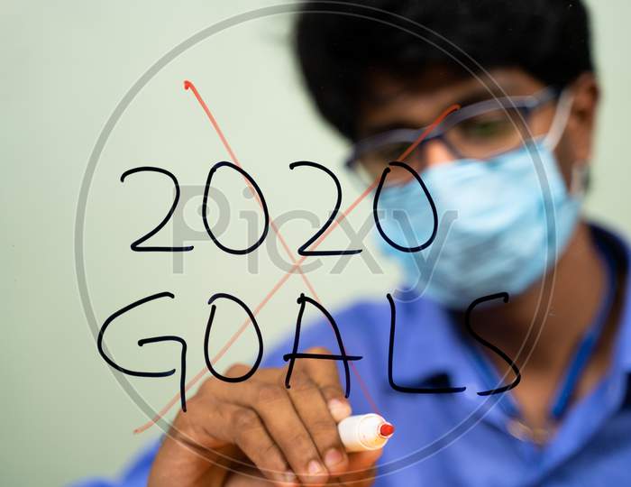 Young Man In Medical Mask Scratching Out 2020 Goals Due To Coronavirus Or Covid-19 Pandemic - Concept Of Failed 2020 Goals.