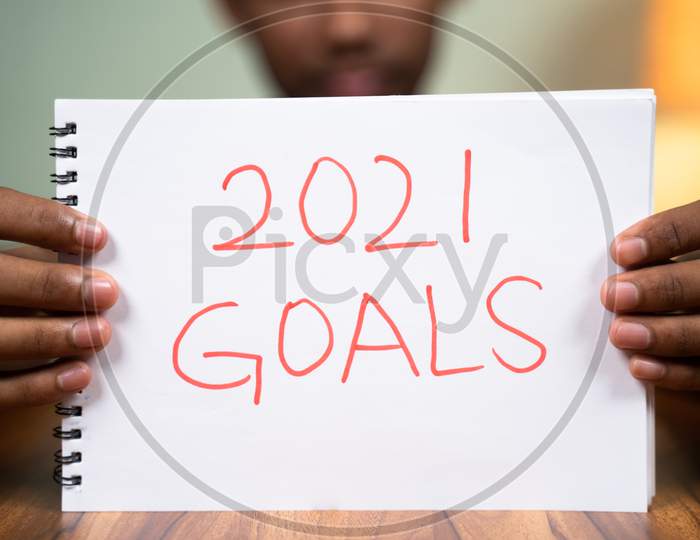 Man On Table Holding 2021 Goals Book In Front Of Camera - Concept Of Planning 2021 New Year Goals.
