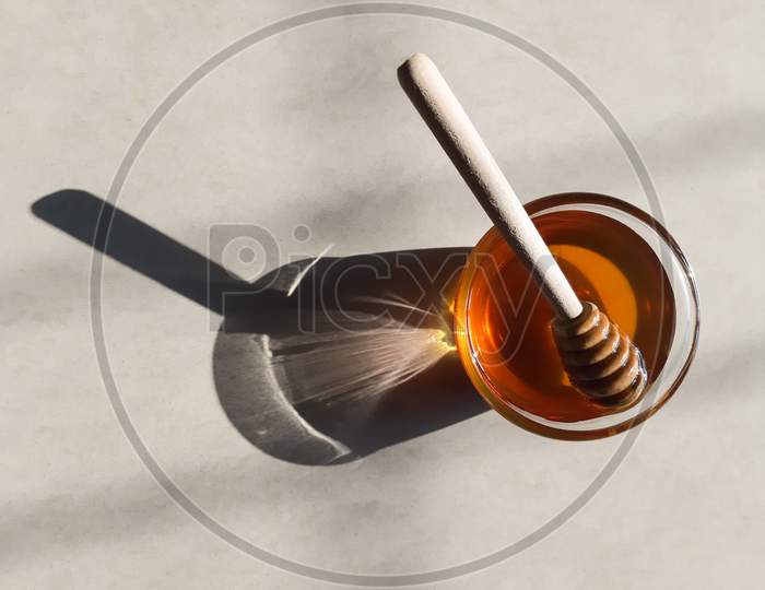 Wooden Honey Dipper In Honey On Off-White Background In Natural Sunlight.Fresh Honey In Glass Bowl With Wooden Honey Stick.