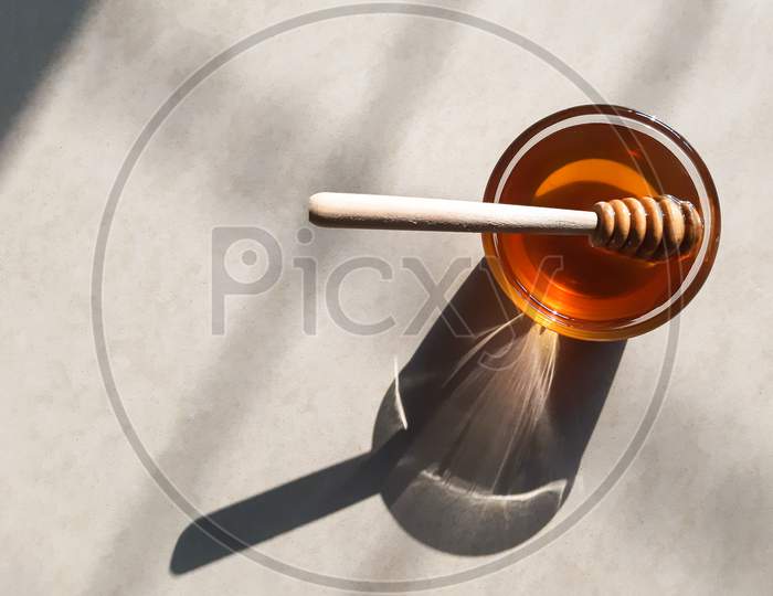 Wooden Honey Dipper In Honey On Off-White Background In Natural Sunlight.Fresh Honey In Glass Bowl With Wooden Honey Stick.