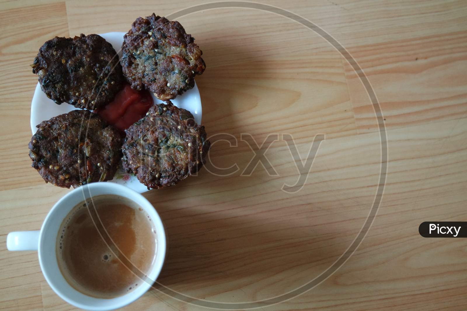 Delicious Spicy Fried Round Kebab Served In White Plate With Cup Of Hot Tea.