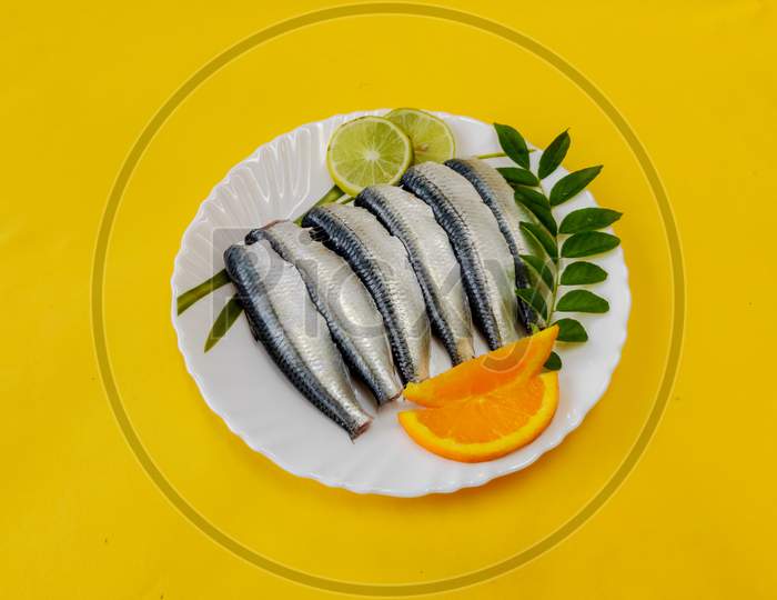 Cleaned And Ready To Cook Fresh Indian Sardine Decorated With Curry Leaves,Lemon Slice And Tomato Slice .Isolated On Yellow Background.