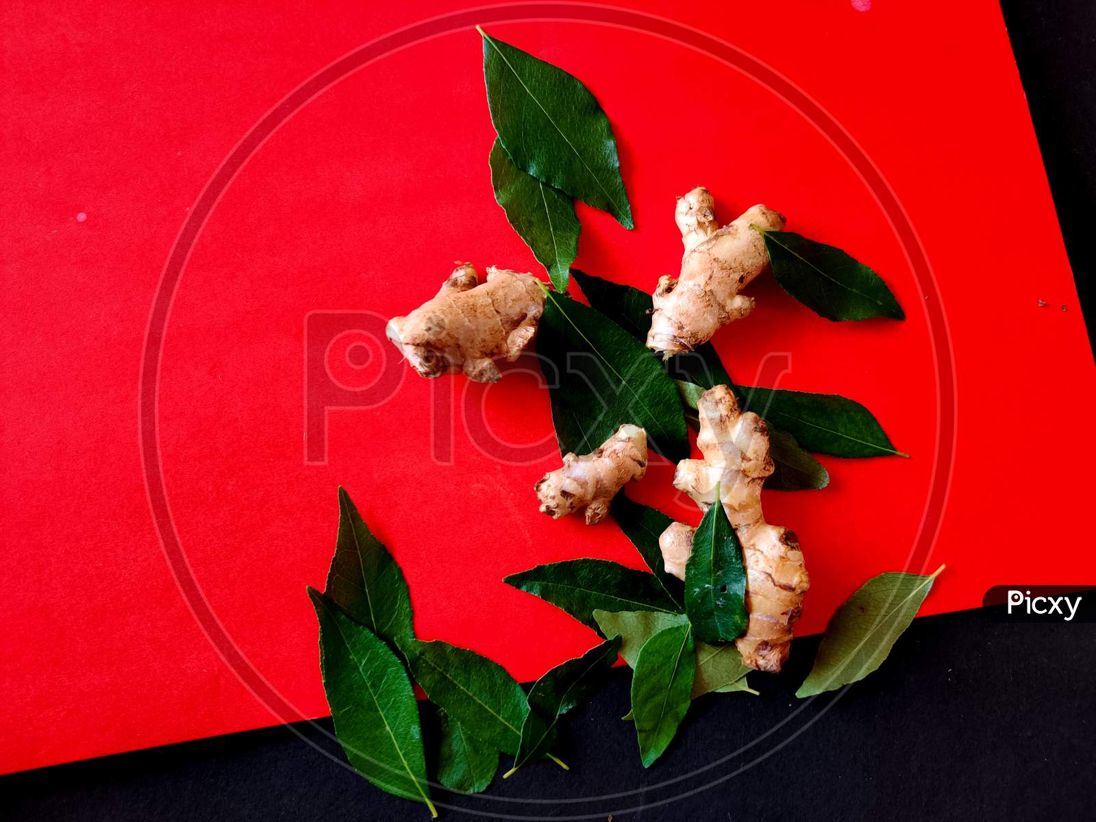 Small Pieces Of Gingers Surrounded With Curry Leaves On A Red Background. Selective Focus