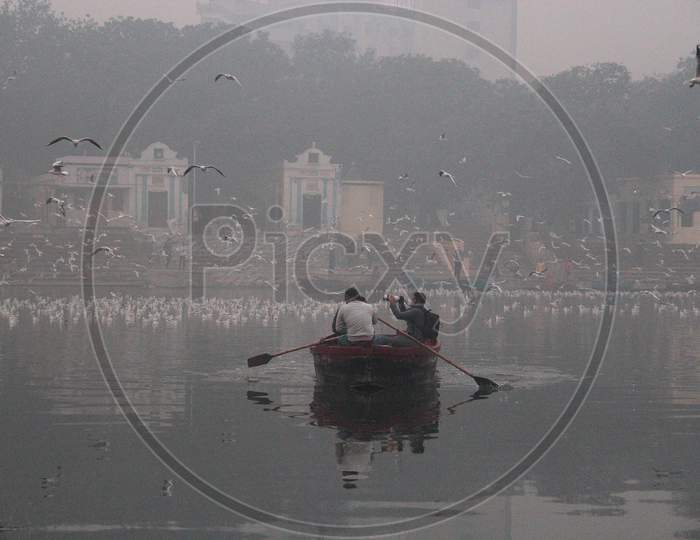 A man clicks photographs while riding a boat as a flock of birds fly over the Yamuna river on a smoggy morning in New Delhi, November 9, 2020.