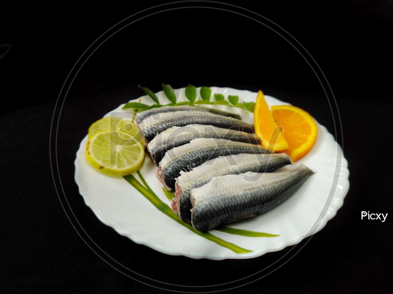 Cleaned And Ready To Cook Fresh Indian Sardine Decorated With Curry Leaves,Lemon Slice And Tomato Slice .Isolated On Black Background.