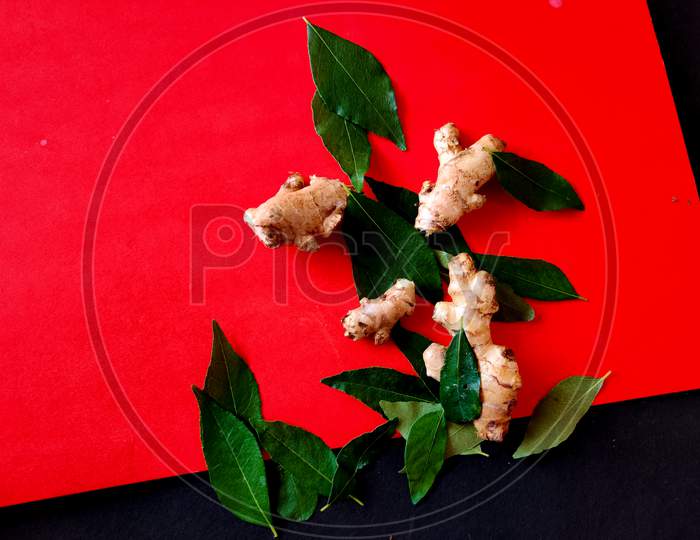 Small Pieces Of Gingers Surrounded With Curry Leaves On A Red Background. Selective Focus
