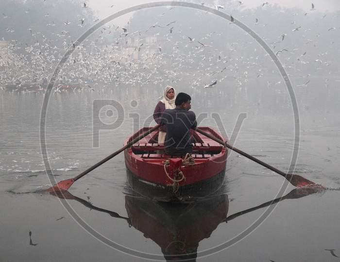 A man rides a boat as a flock of birds fly over the Yamuna river on a smoggy morning in New Delhi, November 9, 2020.