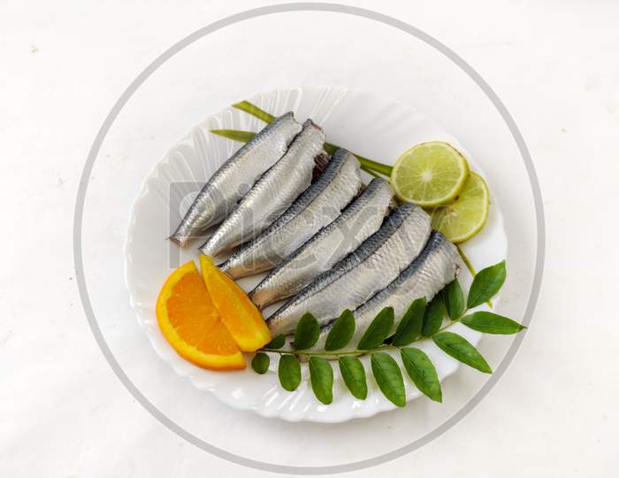Cleaned And Ready To Cook Fresh Indian Sardine Decorated With Curry Leaves,Lemon Slice And Tomato Slice .Isolated On White Background.