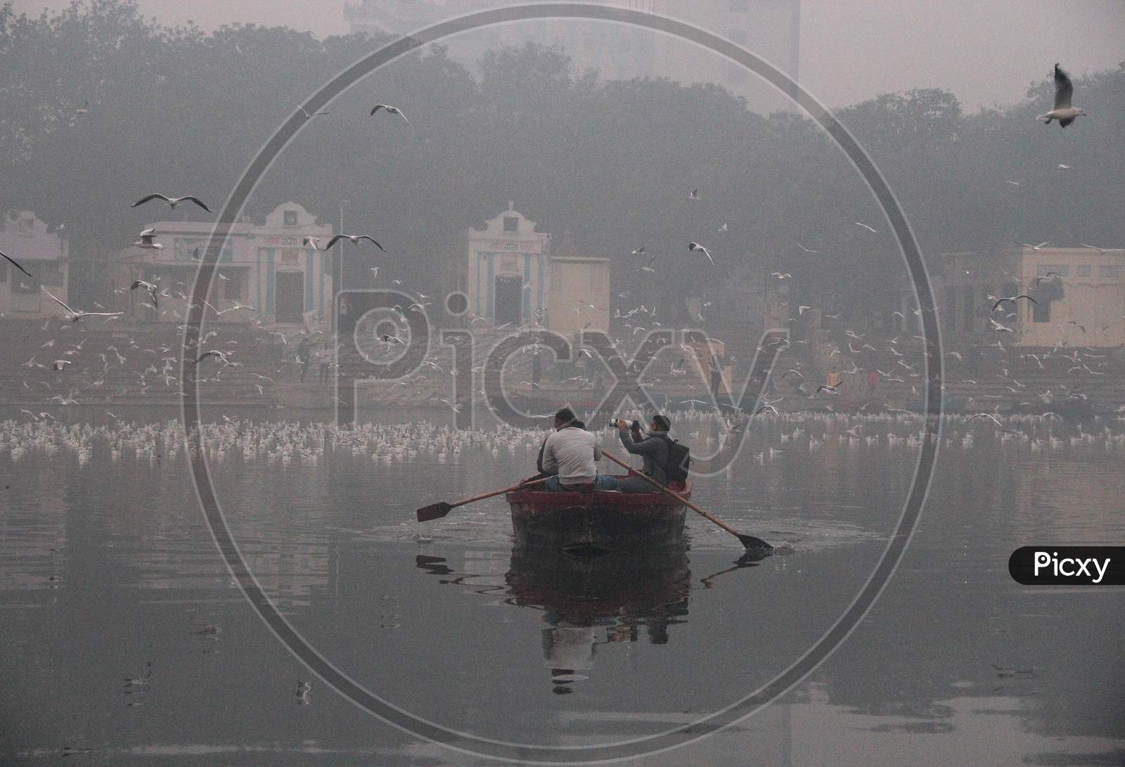 A man clicks photographs while riding a boat as a flock of birds fly over the Yamuna river on a smoggy morning in New Delhi, November 9, 2020.
