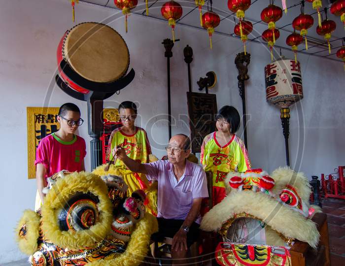 An Old Man Clean The Lion Dance Head With Brush With Accompanied By Teenagers