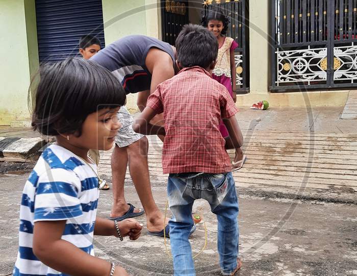 Closeup of different age group kids playing Buguri or Spinning Tops on Roadside during holiday