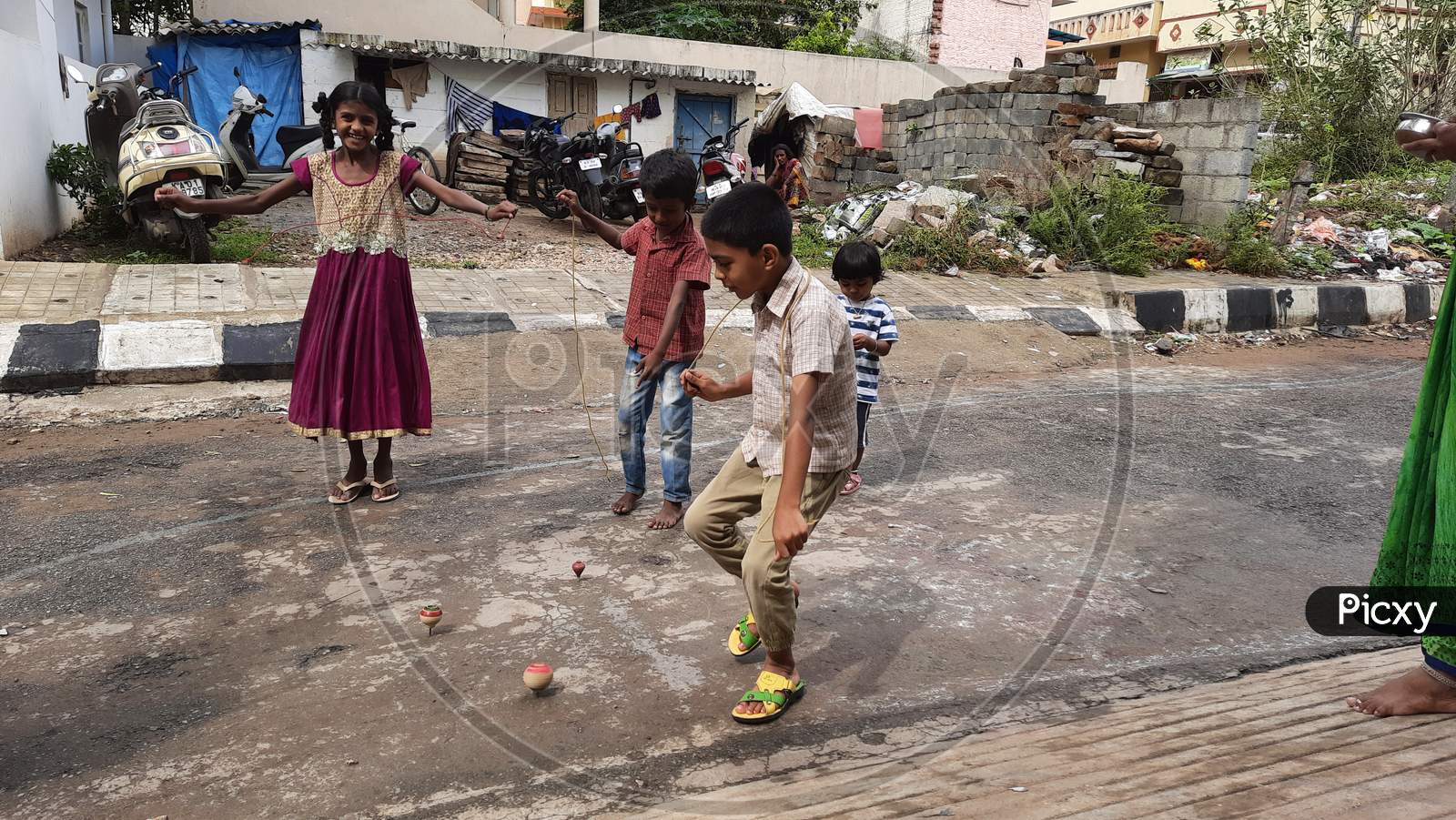Closeup of different age group kids playing Buguri or Spinning Tops on Roadside during holiday