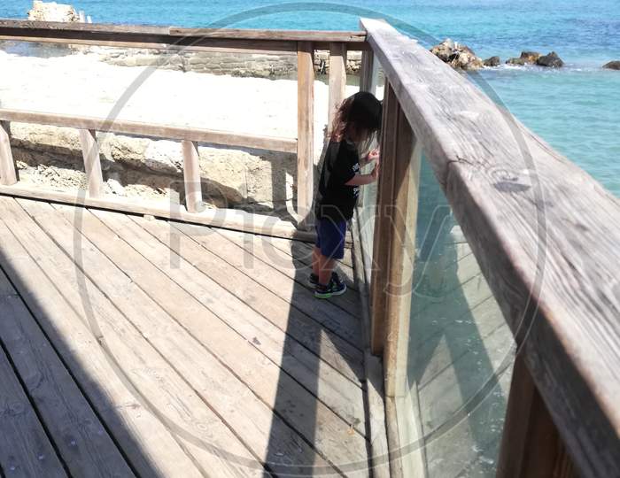 Child boy standing on Dock Against the Sea and enjoying seashore