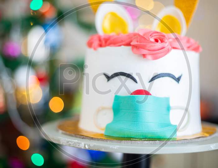 Christmas cake, deer wearing mask design, celebration during covid pandemic concept, blur bokeh christmas decorated tree background , selective focus, holiday and festive season.