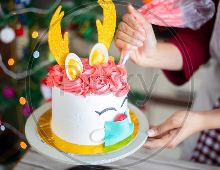 Closeup of hand preparing christmas deer design cake at home, icing butter cream.with piping bag, celebration during covid pandemic, festive holiday season
