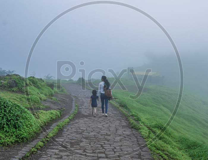 A lady and a kid walking in a misty green mountain