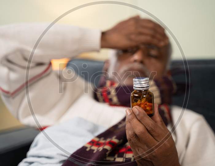 Selective focus on tablet or pills bottle, sick Old man worried about taking pills by placing hand on his head