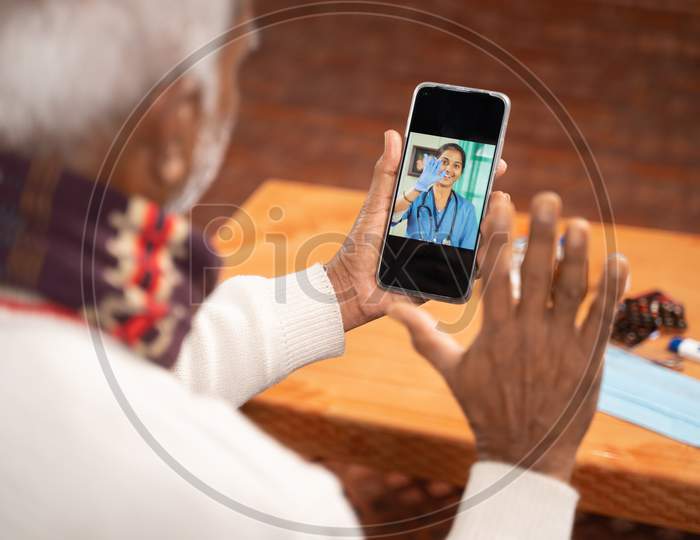 Shoulder shot of Old man on video with to doctor on mobile phone - concept of nurse Online Chat, telehealth, or tele counseling during coronavirus or covid-19 pandemic