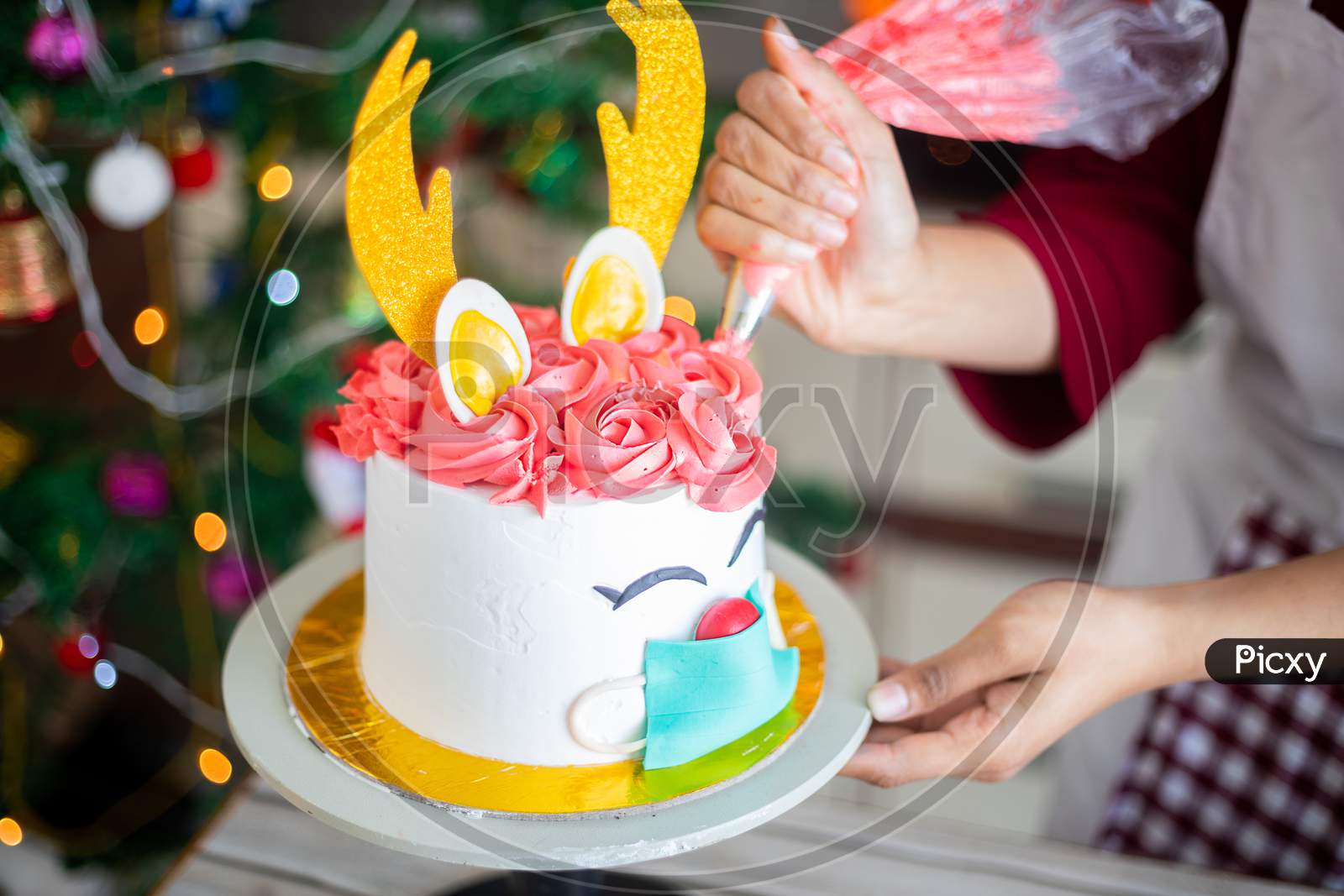 Closeup of hand preparing christmas deer design cake at home, icing butter cream.with piping bag, celebration during covid pandemic, festive holiday season