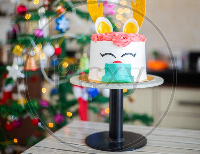 Christmas cake, deer wearing mask design, celebration during covid pandemic concept, blur bokeh christmas decorated tree background , selective focus, holiday and festive season.