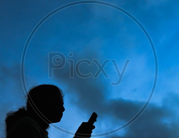 Silhouette of a lady holding a mobile phone with blue sky in the background
