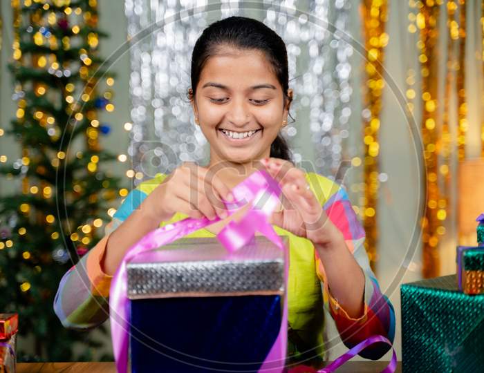 Concept Showing Of Girl Busy In Opening Gift Box During Christmas Eve With Xmas Decorated Background At Home - Concept Of Self Gifting Or Christmas Presents.