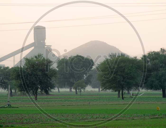 Panning Shot Of Green Natural Feild With Large Trees Fading Off Into The Foggy Distance And The Silhouette Of A Factory In The Distance Showing The Mixing Of Rural Agricultural Lift And Manufacturing In Smaller Indian Towns And Villages