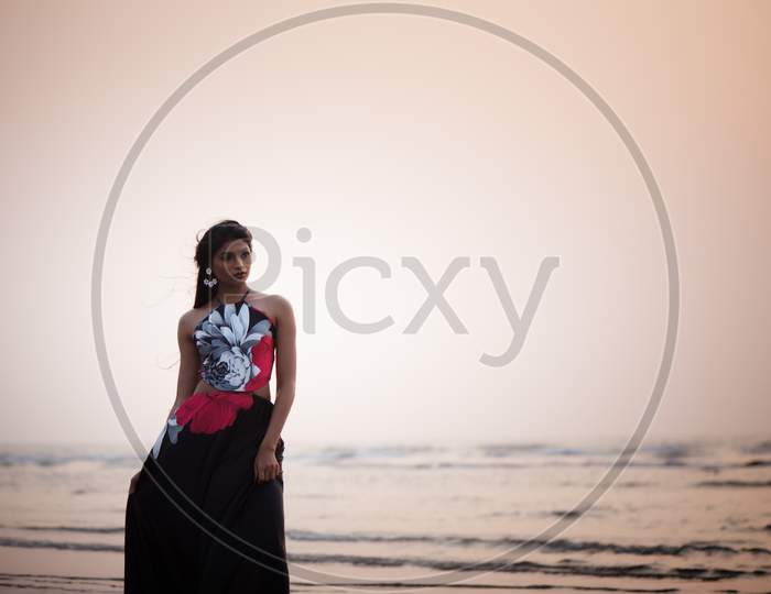Lifestyle of young Indian woman enjoying her vacation on beach during sun set and wearing black one-piece gown