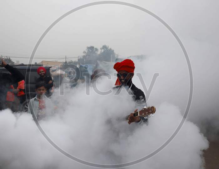 A protester plays guitar amid smoke during fumigation of an area at Singhu border where farmers are camped in an ongoing protest against the Centres new farm laws on December 11, 2020 near New Delhi, India.