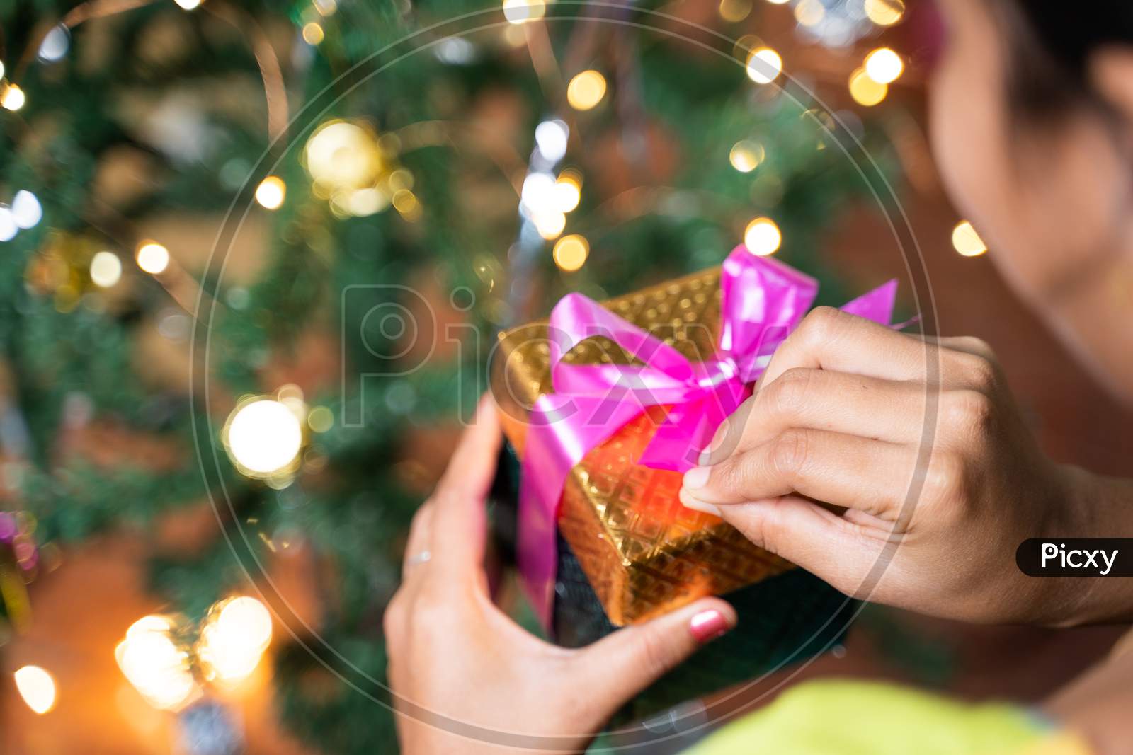 Concept Of Self Gifting During Holiday Shopping Or Celebration - Shoulder Shot Of Girl Infront Of Decorated Christmas Tree Opening Gift Box.