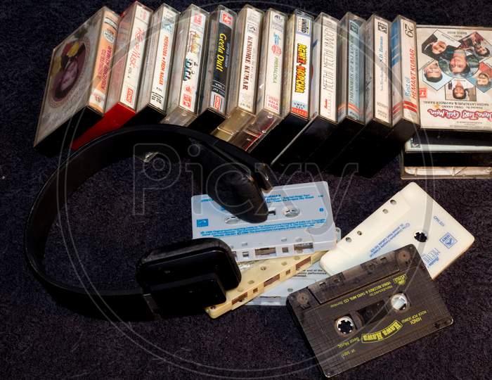 A beautiful collection of old Music Audio cassette tapes with their containers and a Wireless Headphone on a Music shelf at Home.