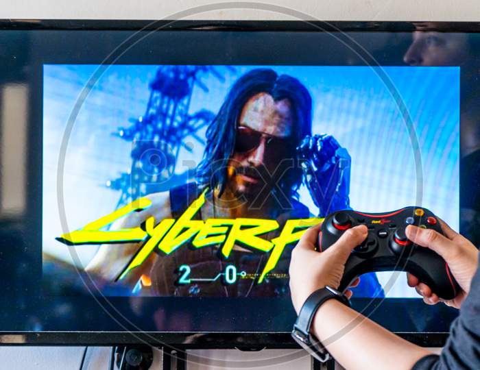 Woman Holding A Generic Controller And Playing Popular Video Game Cyberpunk 2077 On A Television And Pc