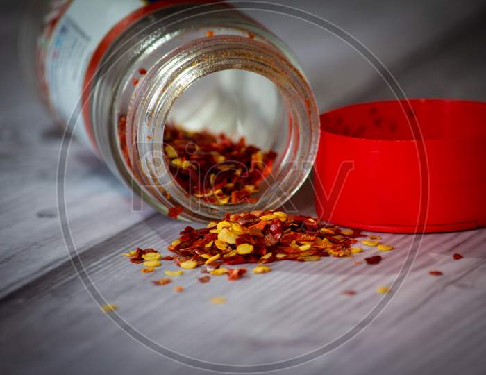 View Of Chilli Flakes Spilled Out Of A Bottle. Red Chili Flakes In A Bottle.