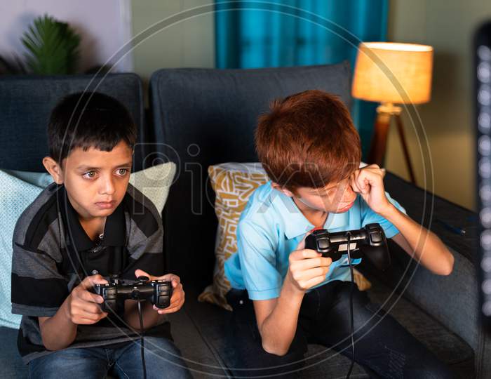 Concept Of Eye Strain Due To Over Night Video Game Play - Two Kids Playing Video Game During Late Night At Home And One Kid Rubbing His Eyes Due Eye Irritations.