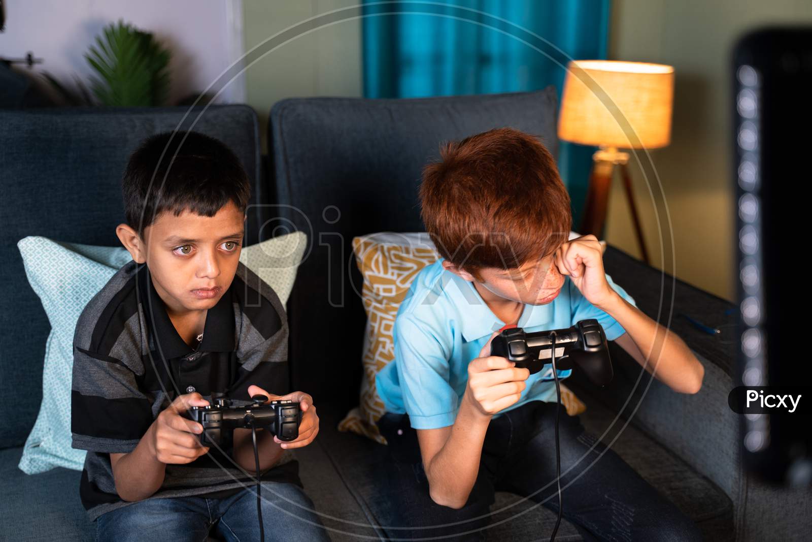 Concept Of Eye Strain Due To Over Night Video Game Play - Two Kids Playing Video Game During Late Night At Home And One Kid Rubbing His Eyes Due Eye Irritations.
