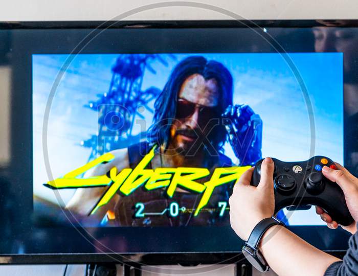 Woman Holding A Xbox Controller And Playing Popular Video Game Cyberpunk 2077 On A Television And Pc