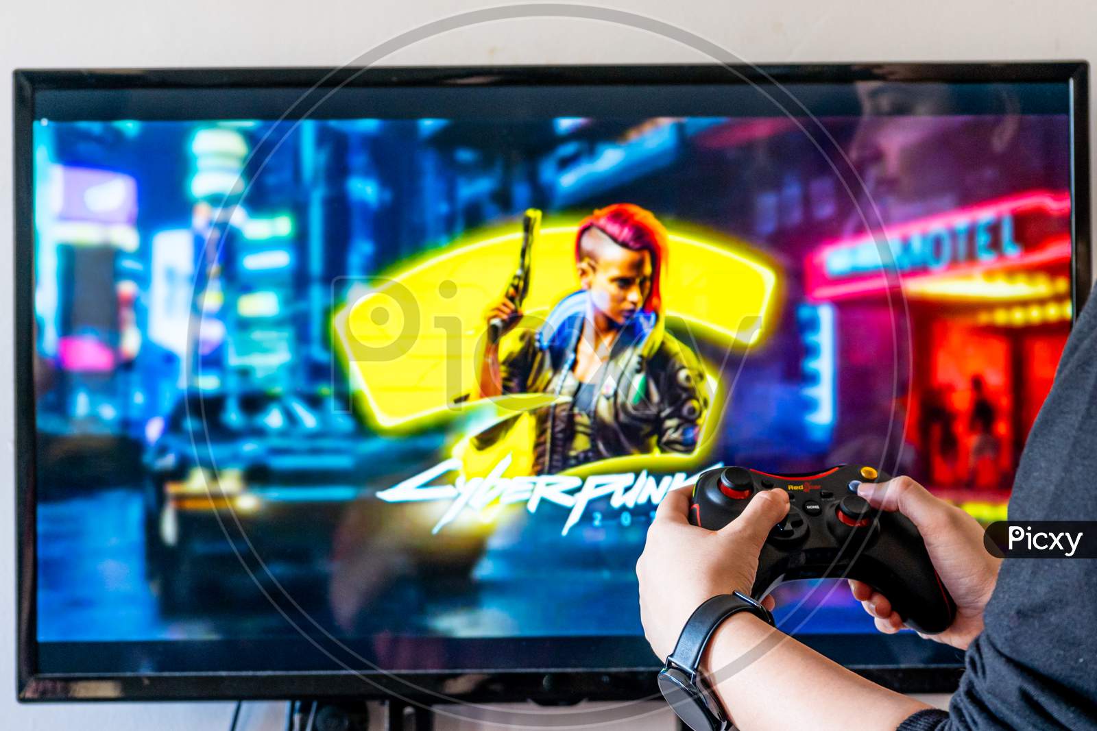 Woman Holding A Red Gear Controller And Playing Popular Video Game Cyberpunk 2077 On A Television And Pc