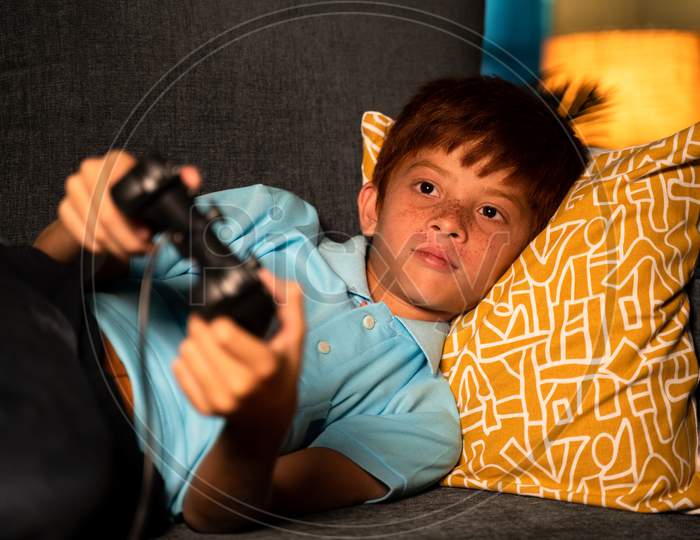 Alone Young Kid Playing Video Game Using Joystick During Late Night While Sleeping On Bed - Concept Of Kids Game Addiction And Late Night Playing Games.