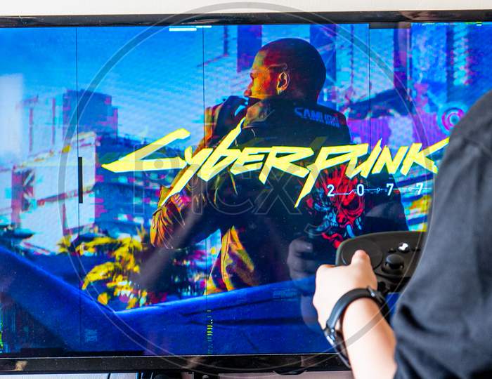 Woman Holding A Steam Controller And Playing Popular Video Game Cyberpunk 2077 On A Television And Pc