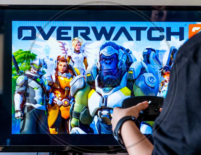 Woman Holding A Steam Controller And Playing Popular Video Game Overwatch On A Television And Pc
