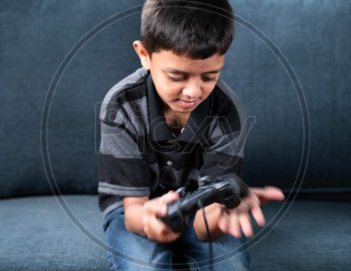 Selective Focus On Kid, Kid Hitting The Gamepad Or Joystick Due To Not Working Properly While Playing Videogame At Home On Sofa.