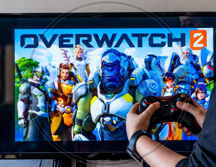 Woman Holding A Generic Controller And Playing Popular Video Game Overwatchon A Television And Pc