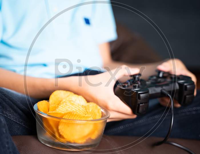 Selective Focus On Snacks, Kid Playing Video Game And Placing Chips To Eat At While Playing At Home During Leisure Time.