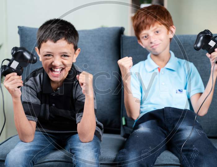 Point Of View Shot, Two Kids Cheering And Shouting After Won The Online Video Game Match While Playing With Joystick Or Gamepad At Home Sitting On Sofa.