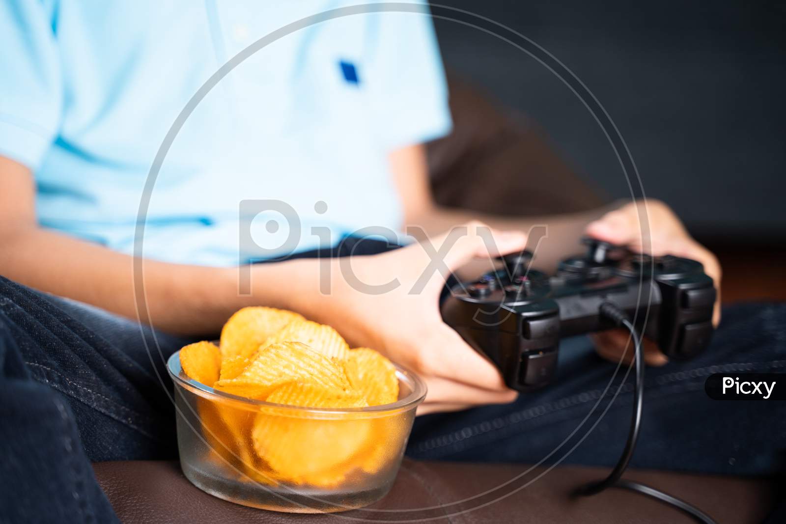 Selective Focus On Snacks, Kid Playing Video Game And Placing Chips To Eat At While Playing At Home During Leisure Time.
