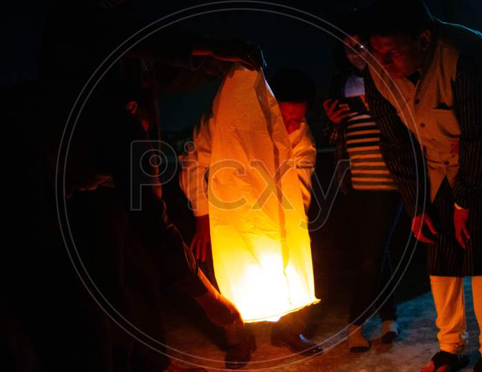 People Holding A Yellow Sky Lantern With The Flames Showing Clearly