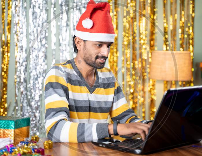 Young Man Busy Working On Laptop During Christmas Or New Year Eve - Concept Of Work From Home During Holiday Season Due To Coronavirus Or Covid-19 Pandemic