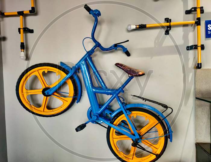 Blue And Yellow Coloured Bicycle Hanging On The Wall